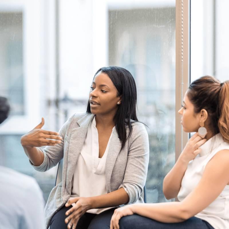 Persoon neemt het woord in een groepsgesprek terwijl anderen luisteren, een moment van spreken ondanks onzekerheid of aarzeling.