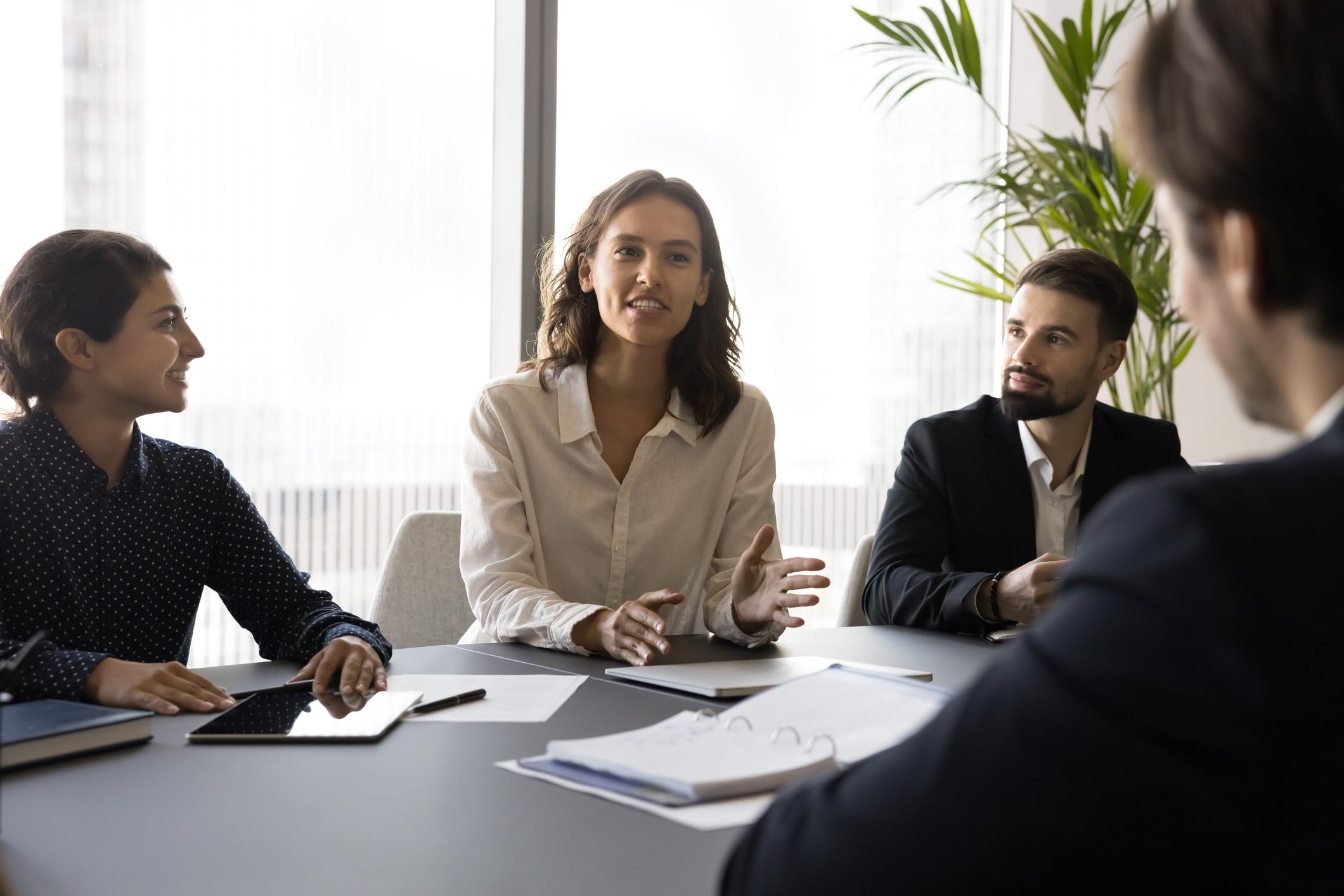 Vier collega's in gesprek aan een vergadertafel. Een vrouw in het midden legt iets uit terwijl de anderen aandachtig luisteren.